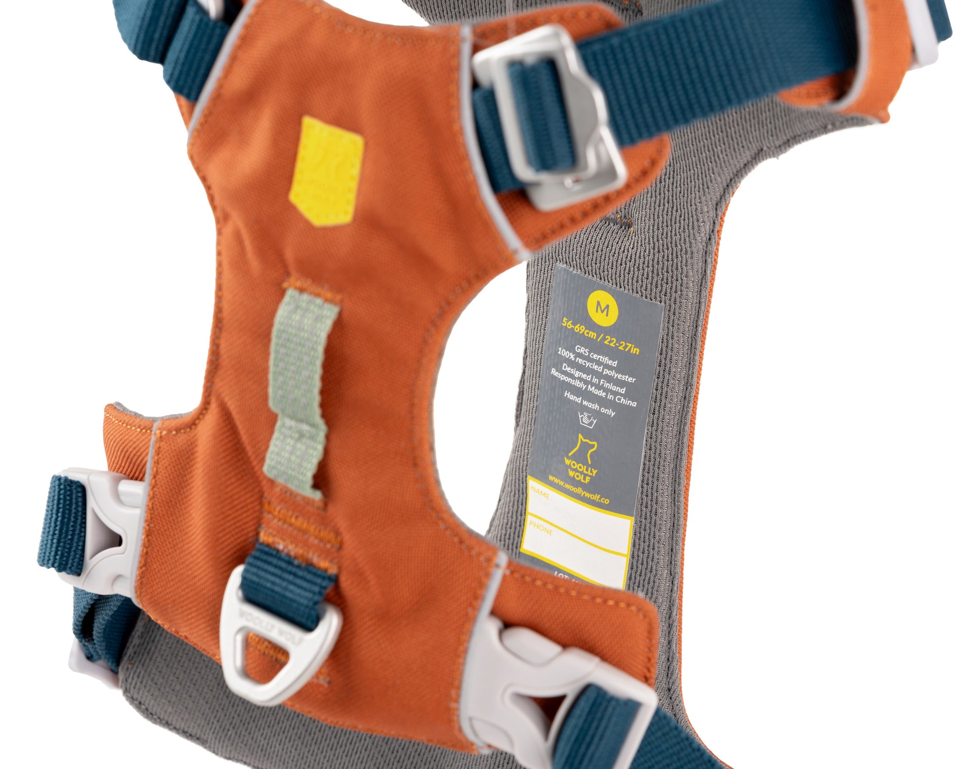 Orange and gray dog harness with adjustable navy straps, white buckles, metal D-ring, and a yellow label indicating size medium, shown against a white background.