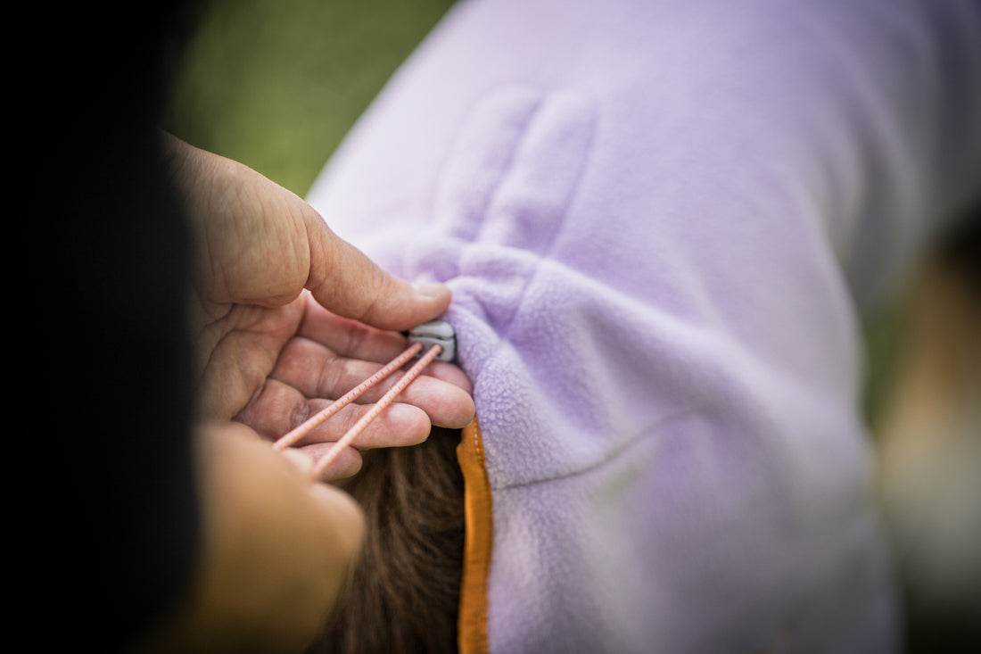 A person adjusting the drawstring on a purple fleece garment.