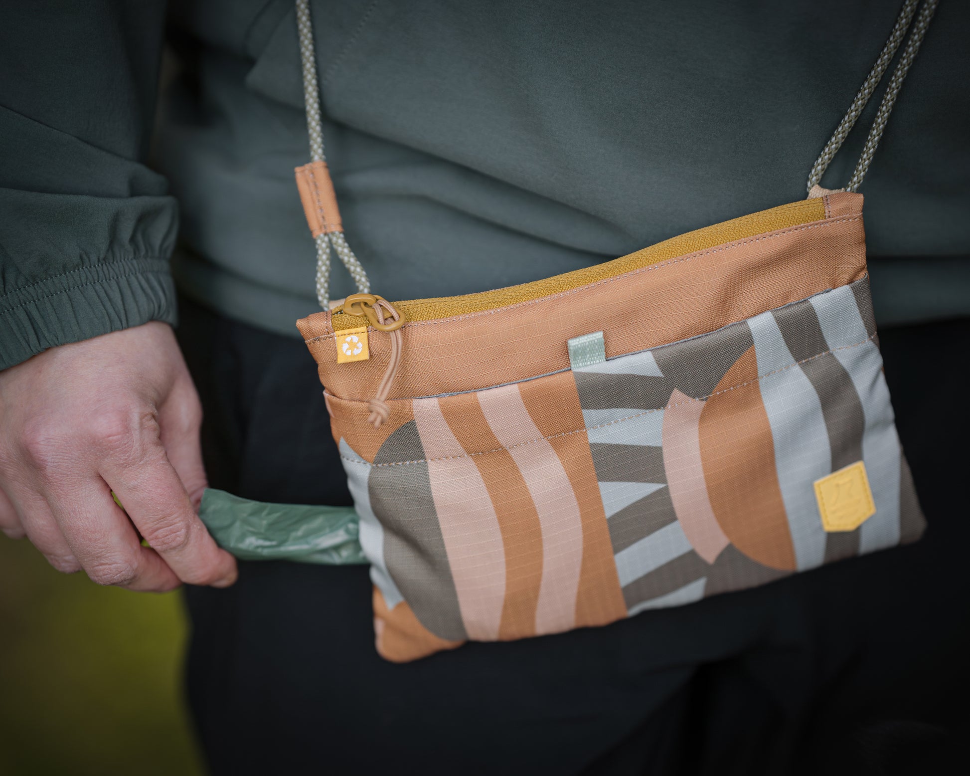A person pulls a green bag from a small crossbody pouch with a geometric pattern.