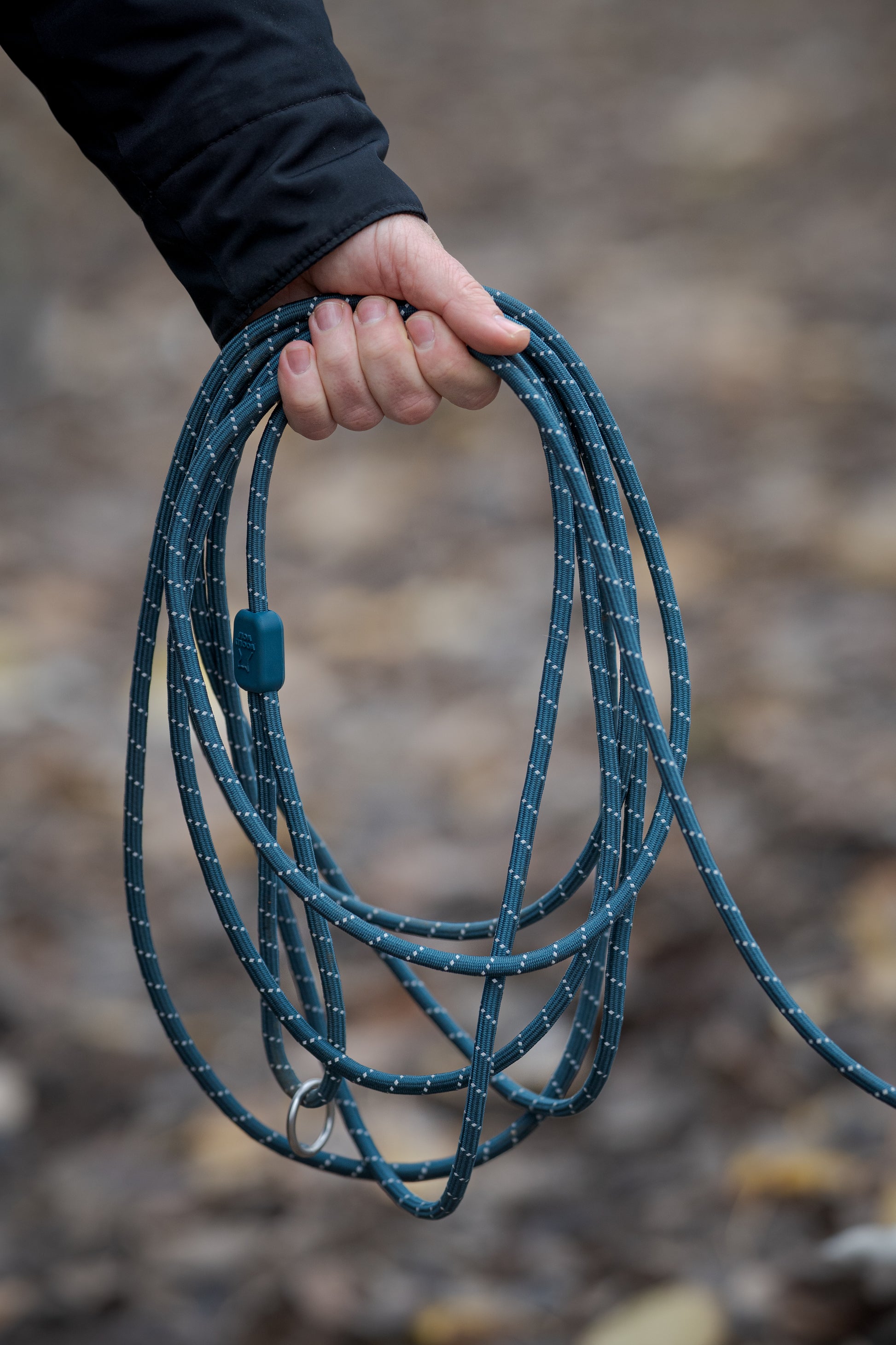 A person holding a coiled blue rope or leash outdoors with a blurred background.