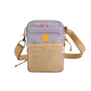 Small crossbody bag with tan strap, tan front pocket, and lavender body, featuring a yellow patch logo.