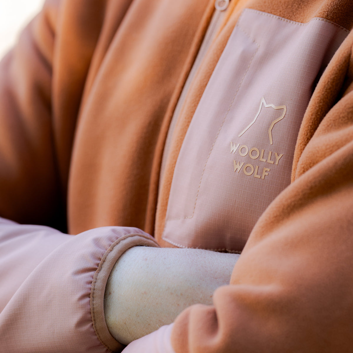 Person wearing a copper-colored fleece jacket with the Woolly Wolf logo on the chest pocket.