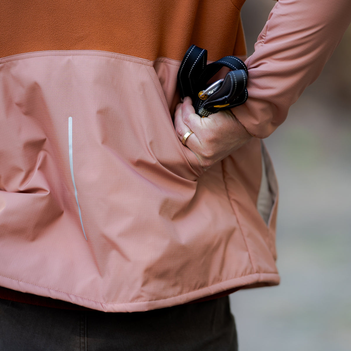 Person in a two-tone jacket with a dog leash tucked into their pocket.