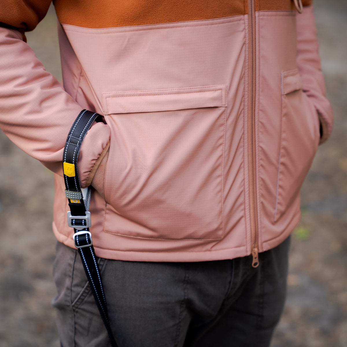 A person wearing a color-blocked jacket with a dog leash tucked into their pocket.