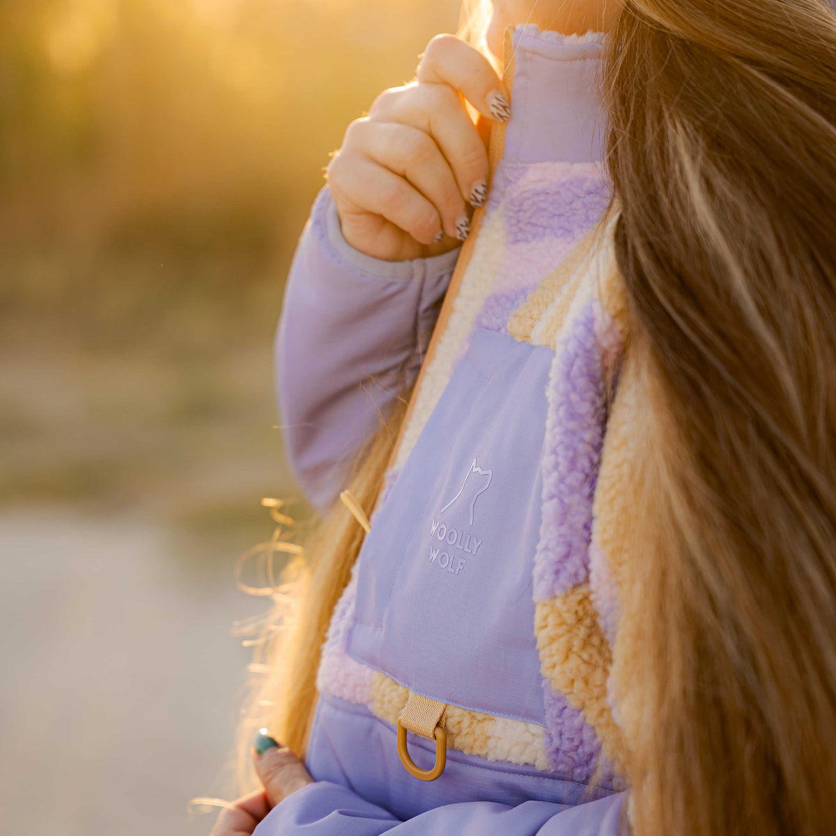 A person wearing a lavender and cream fleece pullover with the Woolly Wolf logo.